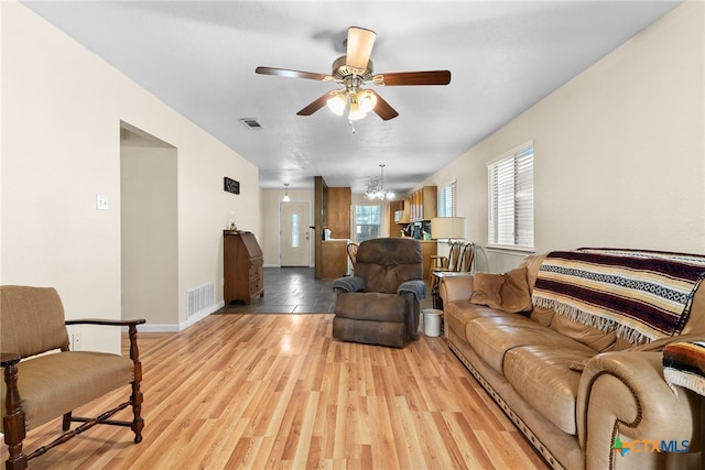 living area with ceiling fan with notable chandelier, baseboards, visible vents, and light wood-style floors