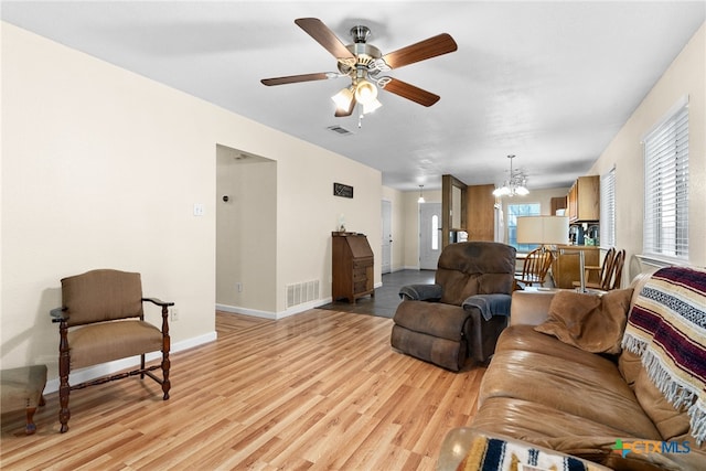 living area with light wood-style flooring, visible vents, baseboards, and ceiling fan with notable chandelier