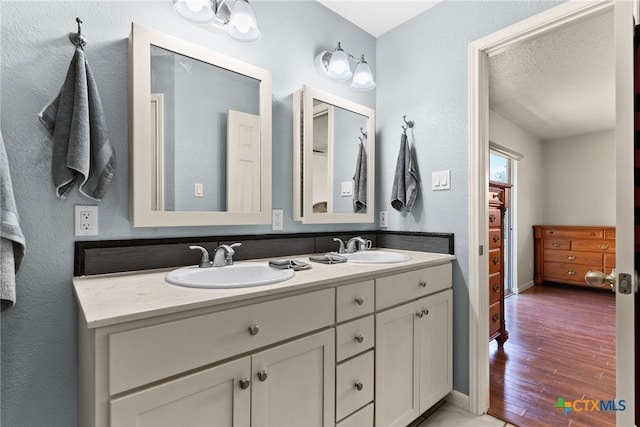 bathroom with double vanity, wood finished floors, a sink, and baseboards