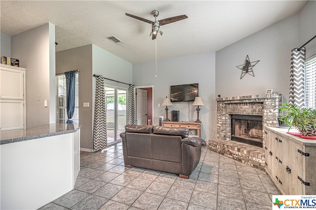 tiled living room with a brick fireplace, a textured ceiling, and ceiling fan