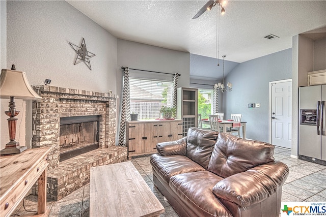 living room with a brick fireplace, ceiling fan with notable chandelier, lofted ceiling, a textured ceiling, and light tile patterned flooring