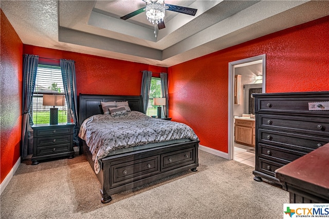 bedroom with ceiling fan, connected bathroom, light carpet, and a tray ceiling