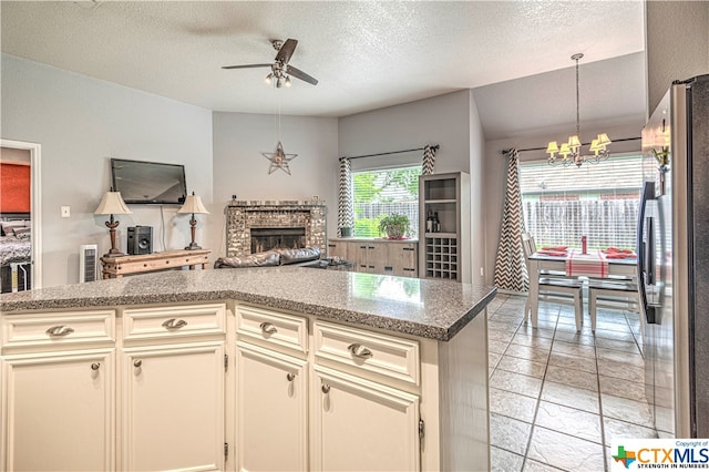 kitchen with a textured ceiling, stainless steel refrigerator, pendant lighting, cream cabinetry, and ceiling fan with notable chandelier