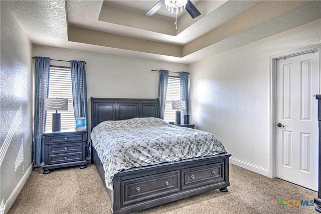 carpeted bedroom featuring multiple windows, a textured ceiling, a raised ceiling, and ceiling fan