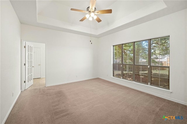 carpeted empty room with ceiling fan and a tray ceiling