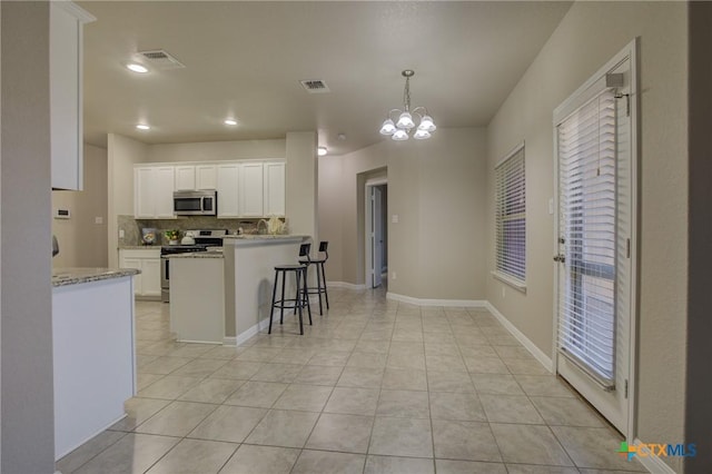 kitchen with decorative light fixtures, a breakfast bar, appliances with stainless steel finishes, white cabinets, and a chandelier