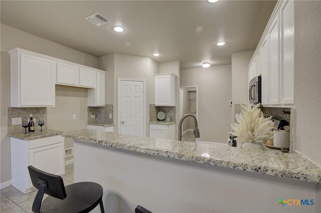 kitchen with a peninsula, stainless steel microwave, tasteful backsplash, visible vents, and light stone counters