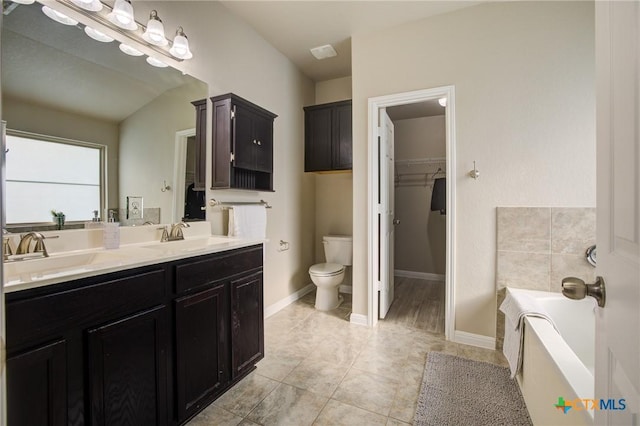 bathroom featuring a walk in closet, a garden tub, toilet, and a sink