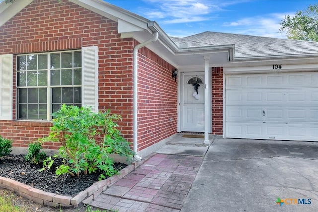 104 Majestic Ln, Victoria, TX 77904 - property entrance with brick siding, an attached garage, a shingled roof, and concrete driveway