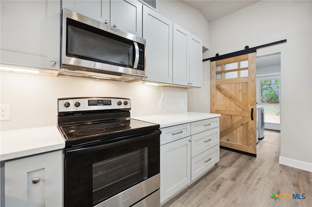 kitchen with a barn door, white cabinetry, stainless steel appliances, and light hardwood / wood-style floors