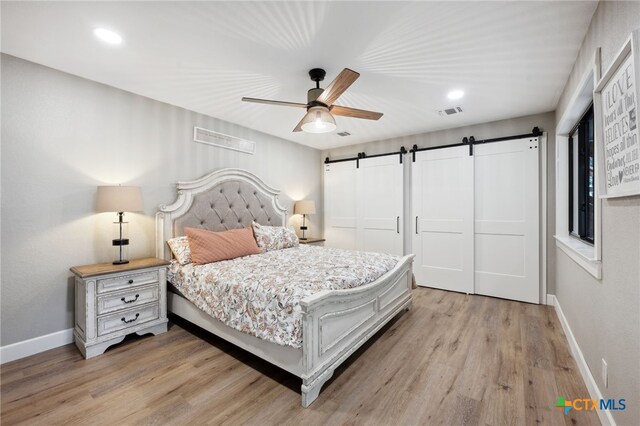 bedroom featuring a barn door, ceiling fan, and light hardwood / wood-style floors