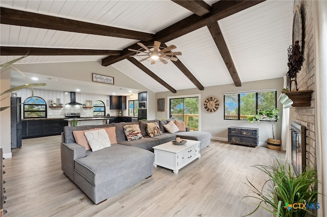 living room featuring ceiling fan, a fireplace, lofted ceiling with beams, and light wood-type flooring