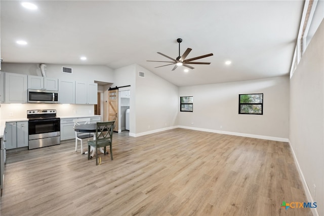 kitchen featuring lofted ceiling, ceiling fan, a barn door, light wood-type flooring, and stainless steel appliances