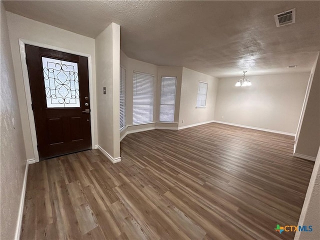 entrance foyer with dark wood-type flooring, a textured ceiling, and an inviting chandelier