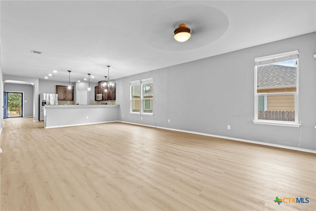 unfurnished living room featuring light wood-type flooring, visible vents, arched walkways, an inviting chandelier, and baseboards