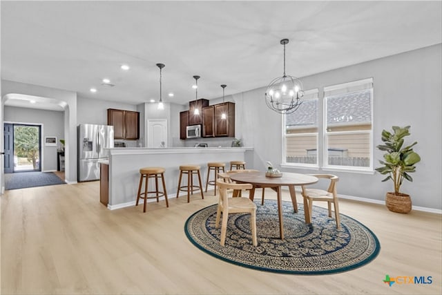 dining room featuring light wood finished floors, baseboards, a chandelier, recessed lighting, and arched walkways