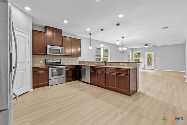 kitchen with hanging light fixtures, light hardwood / wood-style flooring, tasteful backsplash, kitchen peninsula, and stainless steel appliances