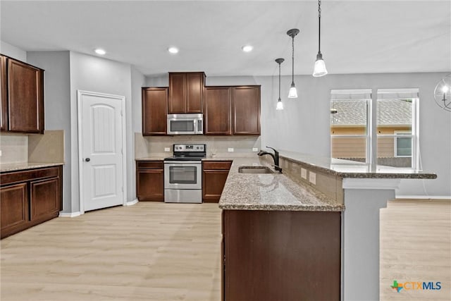 kitchen with light stone counters, light wood-style flooring, appliances with stainless steel finishes, a peninsula, and a sink