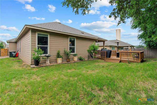 rear view of property featuring a wooden deck, a yard, and fence