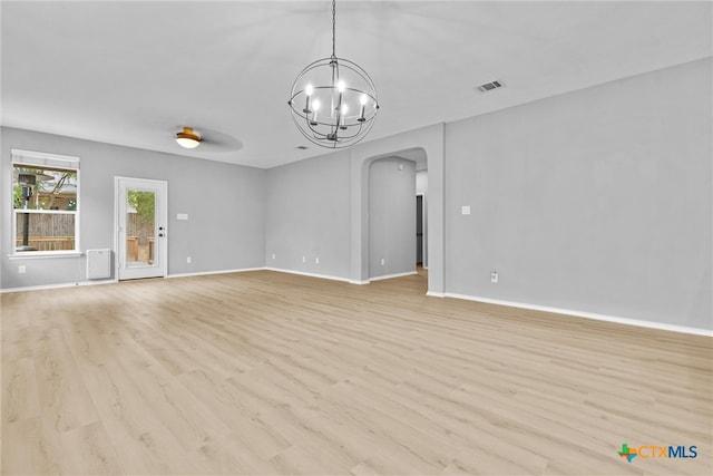 spare room with visible vents, a notable chandelier, arched walkways, light wood-style floors, and baseboards