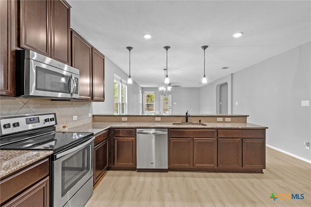 kitchen with tasteful backsplash, light wood finished floors, light stone counters, stainless steel appliances, and a sink