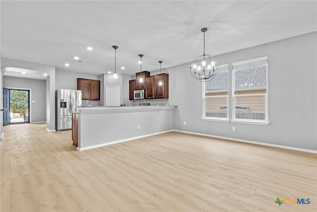 kitchen featuring light wood-style flooring, decorative light fixtures, stainless steel appliances, arched walkways, and a chandelier