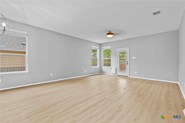 empty room featuring a notable chandelier, visible vents, baseboards, and wood finished floors