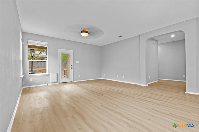 unfurnished room with visible vents, baseboards, arched walkways, and light wood-style flooring