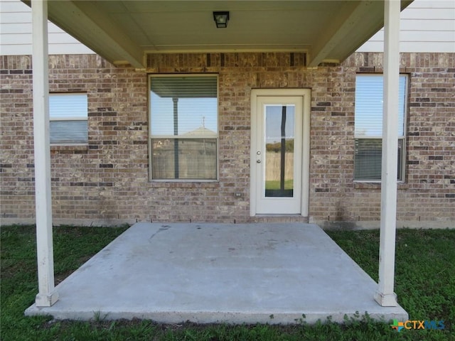 view of exterior entry with a patio and brick siding