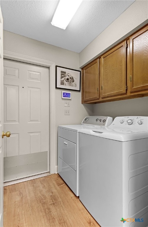 laundry room with cabinets, light hardwood / wood-style floors, a textured ceiling, and washing machine and clothes dryer