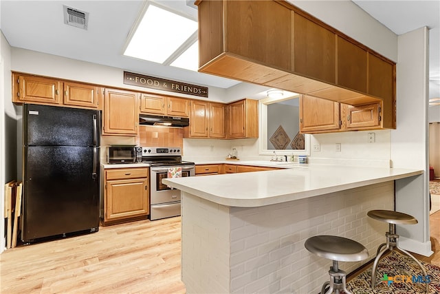 kitchen with black fridge, kitchen peninsula, a kitchen breakfast bar, stainless steel range with electric cooktop, and light wood-type flooring