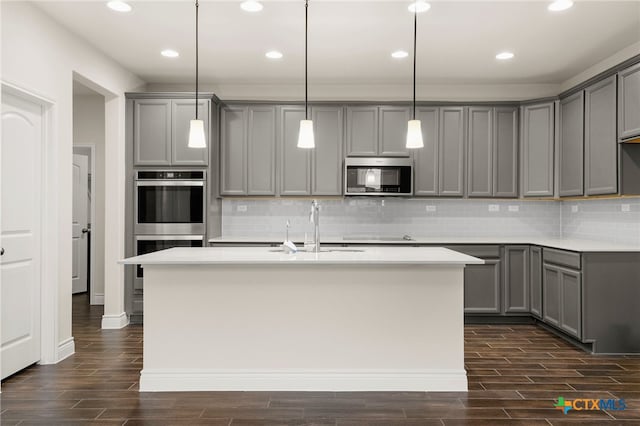 kitchen featuring an island with sink, gray cabinets, stainless steel appliances, pendant lighting, and sink