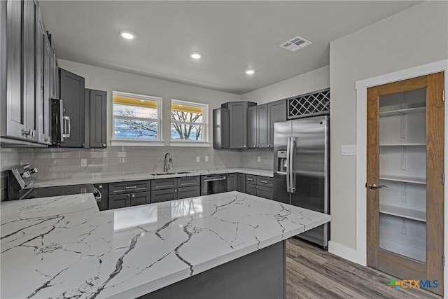 kitchen featuring light stone countertops, tasteful backsplash, sink, dark wood-type flooring, and stainless steel fridge