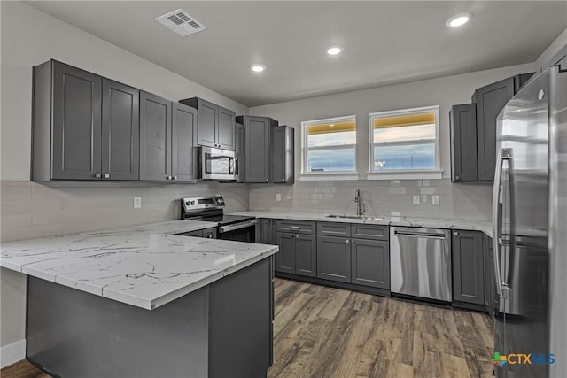 kitchen featuring kitchen peninsula, dark hardwood / wood-style flooring, backsplash, light stone countertops, and stainless steel appliances