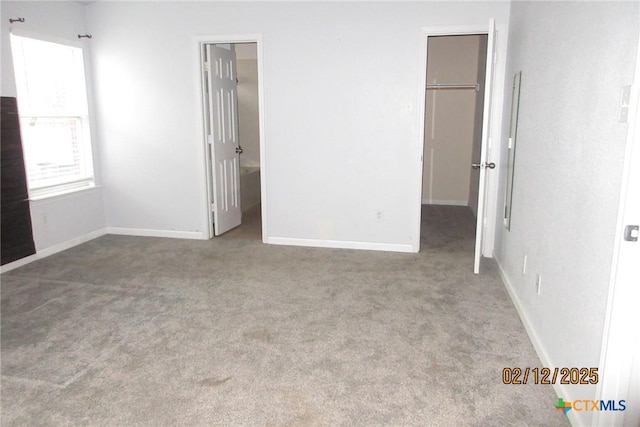 unfurnished bedroom featuring a walk in closet, carpet flooring, and baseboards