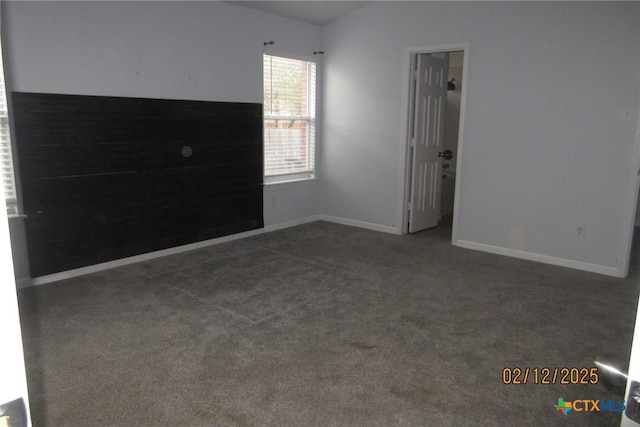 empty room featuring vaulted ceiling, dark carpet, and baseboards