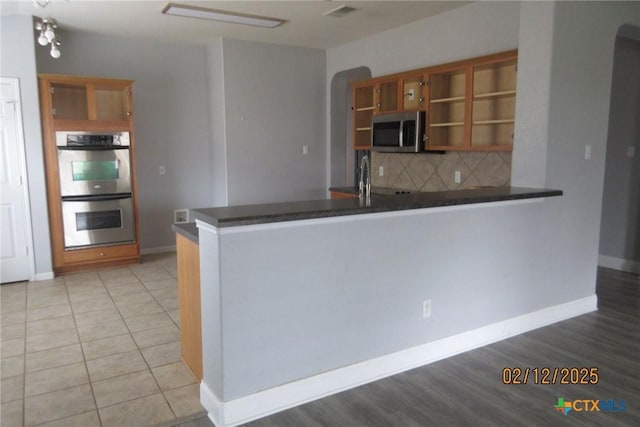 kitchen featuring arched walkways, stainless steel appliances, a peninsula, open shelves, and dark countertops