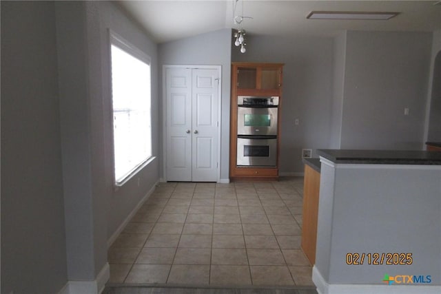 kitchen featuring light tile patterned floors, dark countertops, double oven, vaulted ceiling, and baseboards