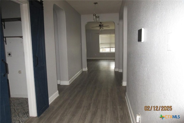 corridor with dark wood-type flooring, arched walkways, and baseboards