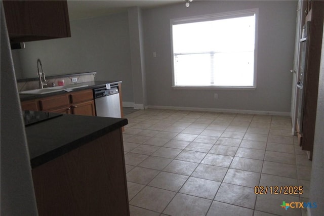 kitchen featuring light tile patterned floors, dark countertops, black electric stovetop, stainless steel dishwasher, and a sink