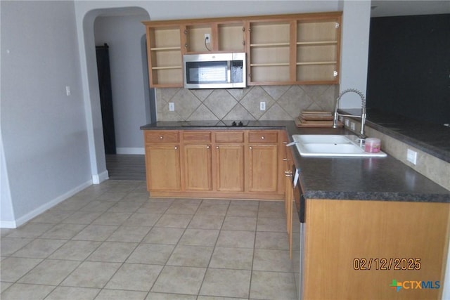 kitchen with a sink, backsplash, open shelves, stainless steel microwave, and dark countertops