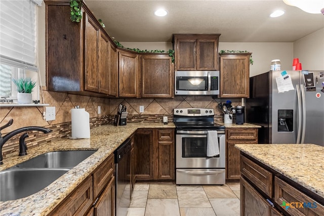 kitchen with tasteful backsplash, appliances with stainless steel finishes, sink, and light stone counters