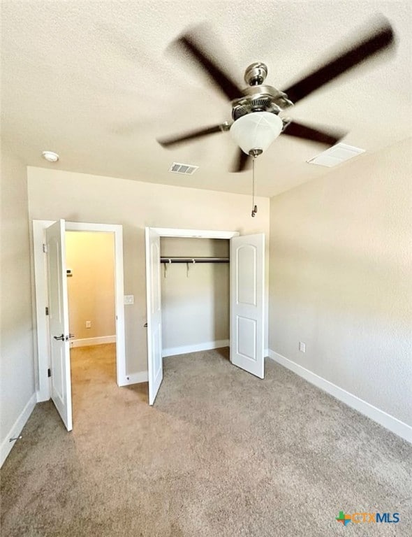 unfurnished bedroom featuring a closet, a textured ceiling, light carpet, and ceiling fan