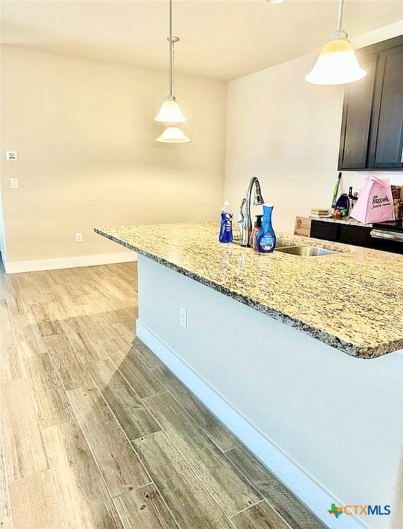 kitchen featuring light stone counters, dark brown cabinets, light hardwood / wood-style flooring, and decorative light fixtures