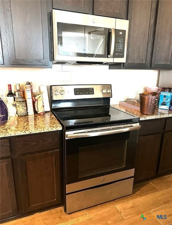 kitchen featuring light stone counters, appliances with stainless steel finishes, dark brown cabinets, and light hardwood / wood-style floors