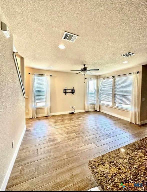 empty room with a wealth of natural light, a textured ceiling, and light hardwood / wood-style floors