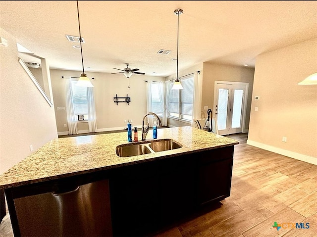 kitchen with light wood-type flooring, sink, decorative light fixtures, and an island with sink