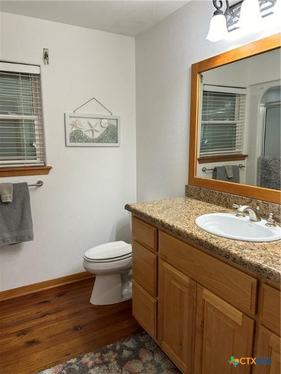 bathroom with vanity, toilet, wood finished floors, and baseboards