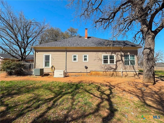 back of house with central AC unit, a lawn, and a chimney