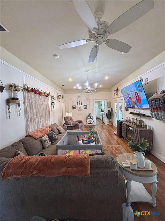 living room with ceiling fan with notable chandelier, wood finished floors, and visible vents